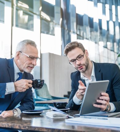 Mature boss and young business man working together using digital tablet in office hall